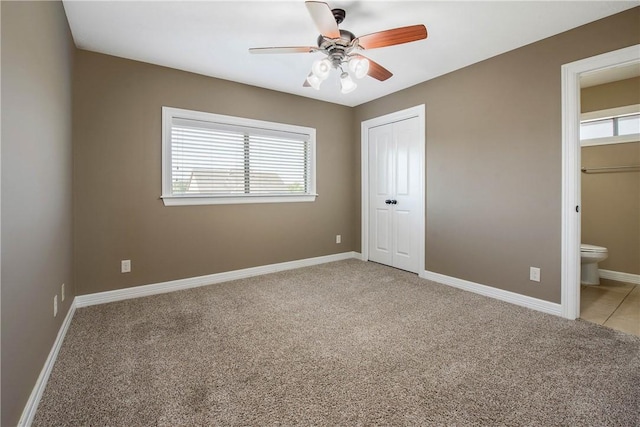 unfurnished bedroom with baseboards, light carpet, ensuite bath, and a ceiling fan