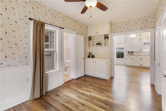 interior space with light wood finished floors, wallpapered walls, light countertops, wainscoting, and white cabinets