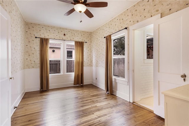 unfurnished room with light wood-type flooring, a wainscoted wall, ceiling fan, and wallpapered walls