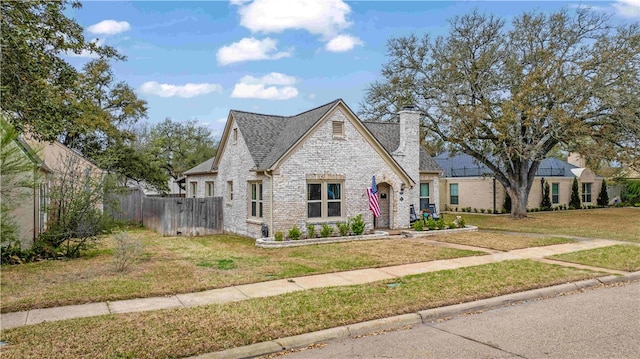 view of front of house with a front yard, fence, a shingled roof, a chimney, and brick siding