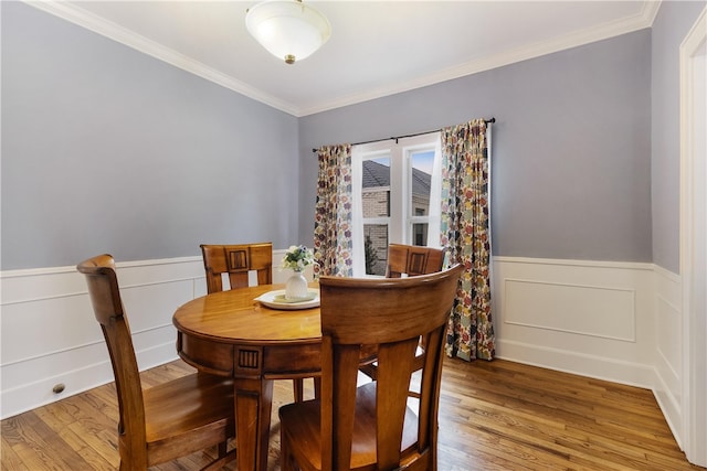 dining area with a wainscoted wall, light wood-style flooring, and crown molding