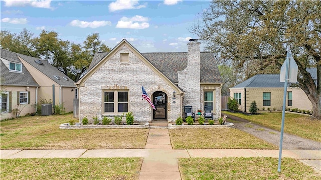 view of front facade featuring brick siding, a chimney, a front lawn, and roof with shingles