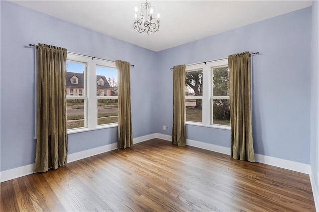 spare room featuring a chandelier, plenty of natural light, and wood finished floors