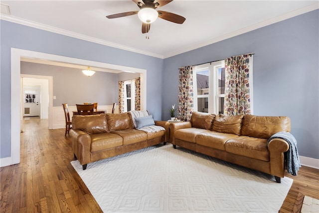 living area featuring a wainscoted wall, light wood-style floors, crown molding, and a ceiling fan