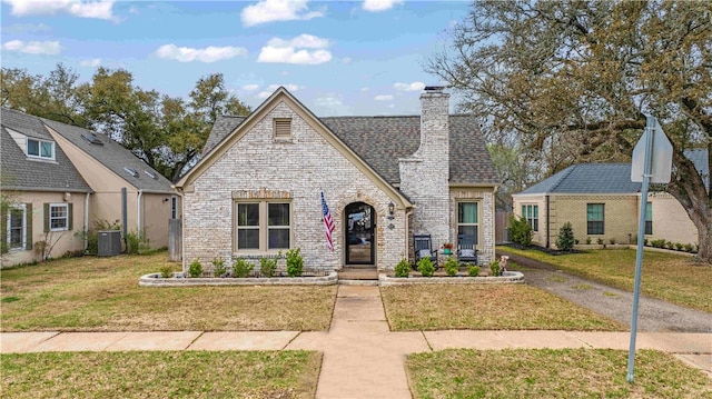 view of front of property with roof with shingles, central AC, a chimney, a front lawn, and brick siding