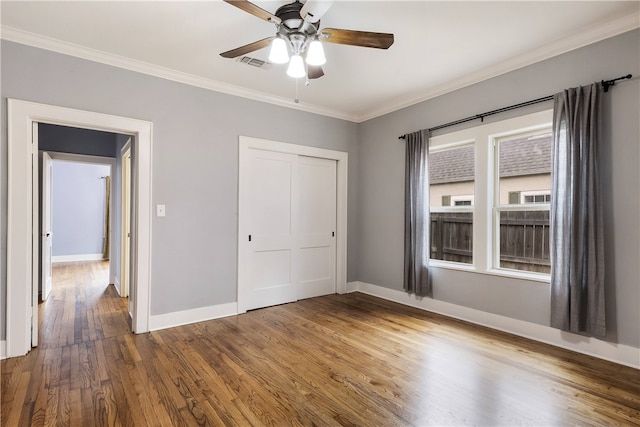 unfurnished bedroom featuring visible vents, crown molding, baseboards, wood finished floors, and a closet