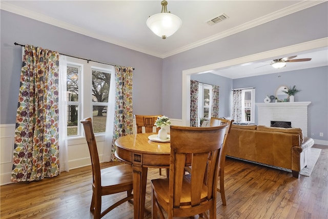 dining room with visible vents, a fireplace, ceiling fan, hardwood / wood-style flooring, and crown molding