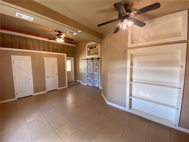 spare room featuring tile patterned floors, ceiling fan, a barn door, and wooden walls