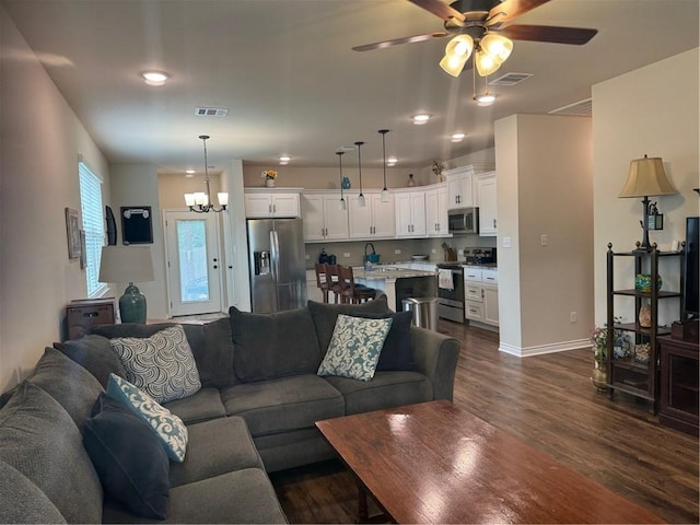 living room featuring visible vents, dark wood finished floors, ceiling fan with notable chandelier, and baseboards