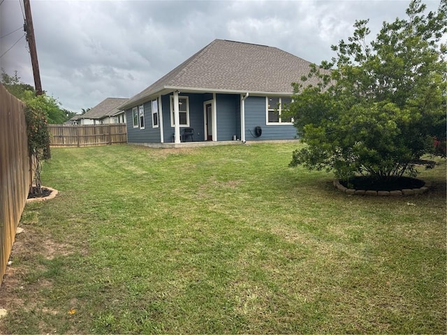 back of property with a lawn, a fenced backyard, and roof with shingles