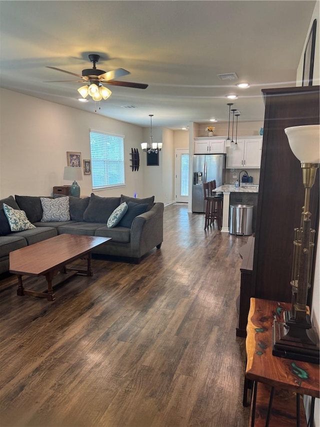 living room featuring dark wood-style flooring, visible vents, and ceiling fan with notable chandelier