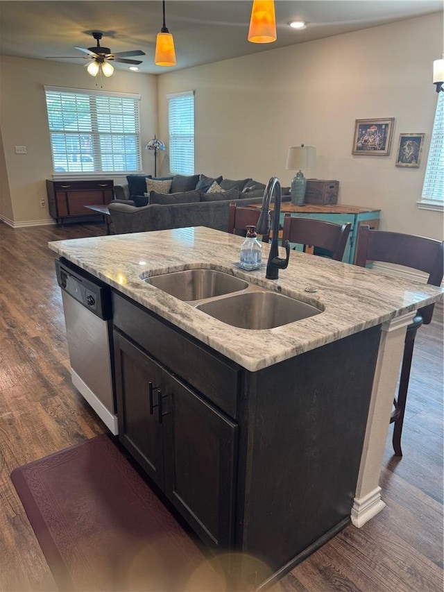 kitchen with pendant lighting, stainless steel dishwasher, a sink, dark wood-type flooring, and an island with sink