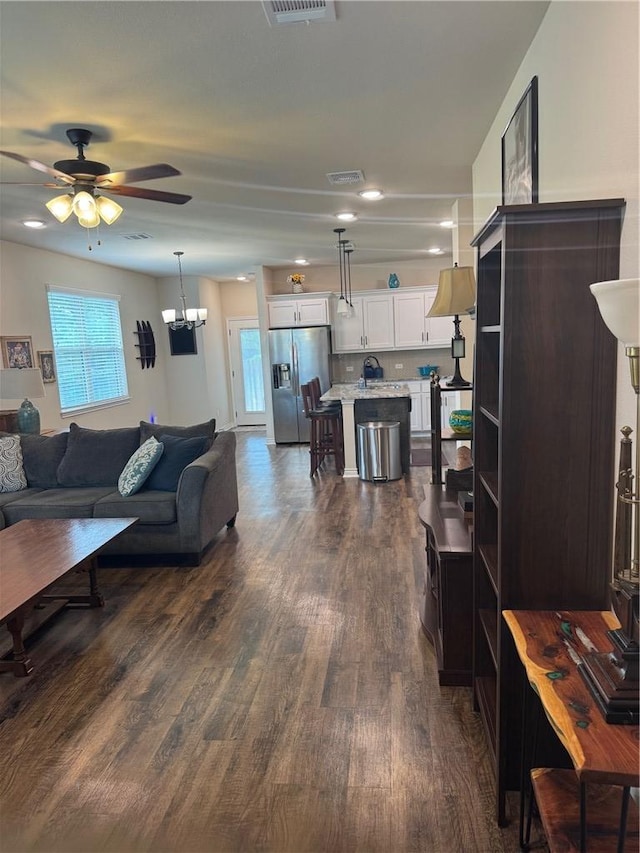 living area featuring visible vents, dark wood-style flooring, and ceiling fan with notable chandelier
