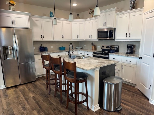 kitchen featuring a kitchen island with sink, stainless steel appliances, a sink, and dark wood-type flooring