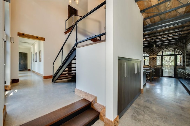 stairway with a high ceiling, finished concrete flooring, and brick wall