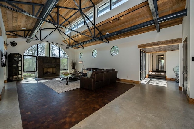 living room featuring baseboards, high vaulted ceiling, concrete flooring, and a fireplace