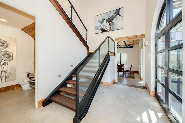 stairway with a high ceiling, baseboards, and concrete flooring