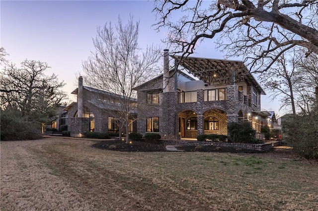 view of front facade featuring brick siding, a chimney, and a front yard