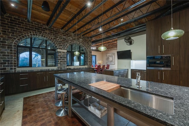 kitchen featuring brick wall, beam ceiling, dark stone counters, dark brown cabinetry, and wood ceiling