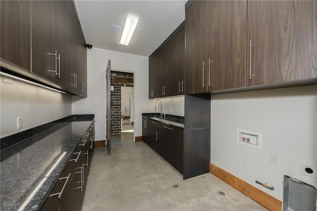 kitchen featuring dark stone countertops, finished concrete flooring, baseboards, a sink, and dark brown cabinets