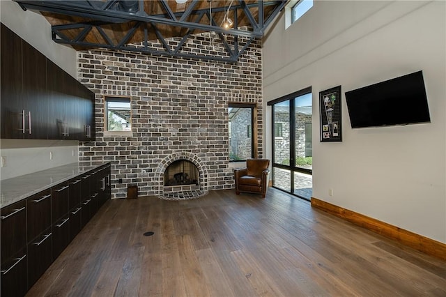 unfurnished living room featuring dark wood-type flooring, a brick fireplace, a healthy amount of sunlight, and baseboards