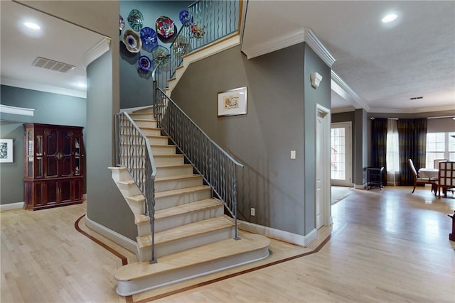 staircase with baseboards, ornamental molding, wood finished floors, and visible vents