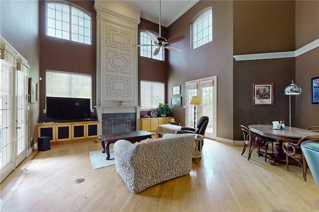 living room with a ceiling fan, a high end fireplace, wood finished floors, ornamental molding, and a high ceiling