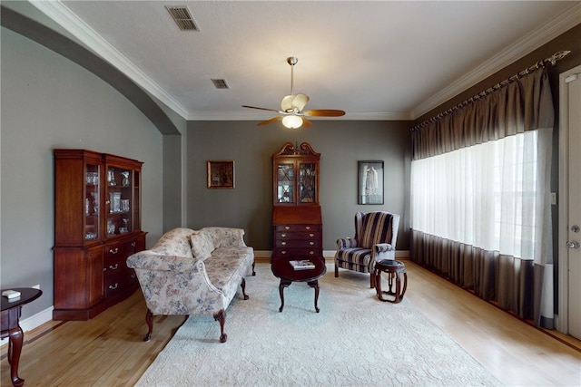 living area with visible vents, ornamental molding, ceiling fan, arched walkways, and light wood finished floors