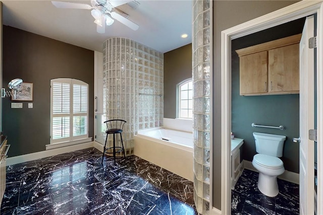 bathroom with marble finish floor, toilet, baseboards, a bath, and a ceiling fan