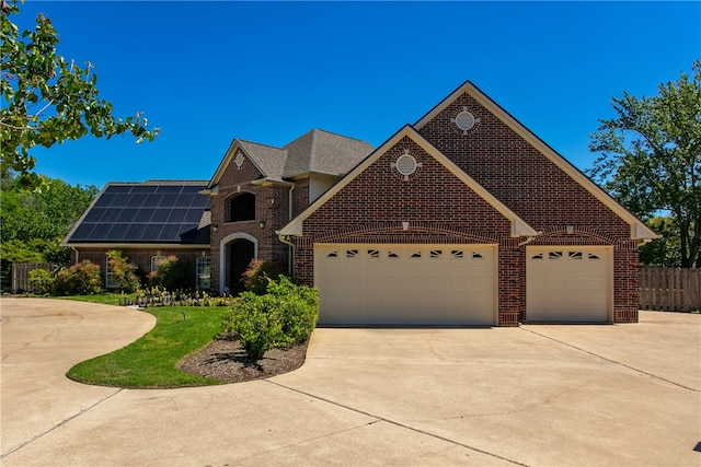 view of front of house with driveway, solar panels, a garage, brick siding, and fence