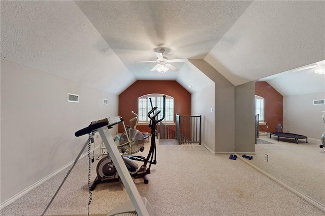 exercise room featuring a ceiling fan, a textured ceiling, visible vents, baseboards, and lofted ceiling