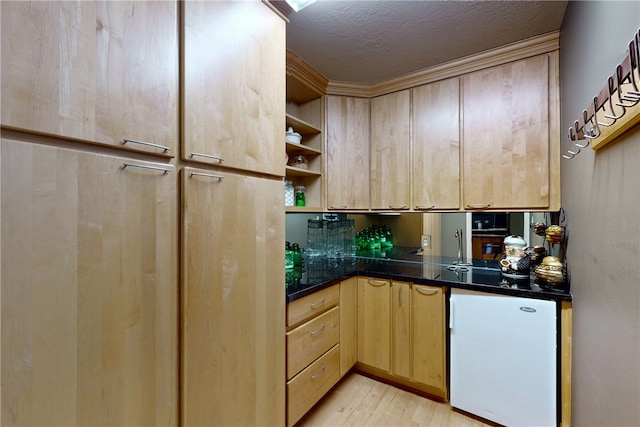 kitchen with light brown cabinetry, fridge, dark countertops, and light wood-type flooring