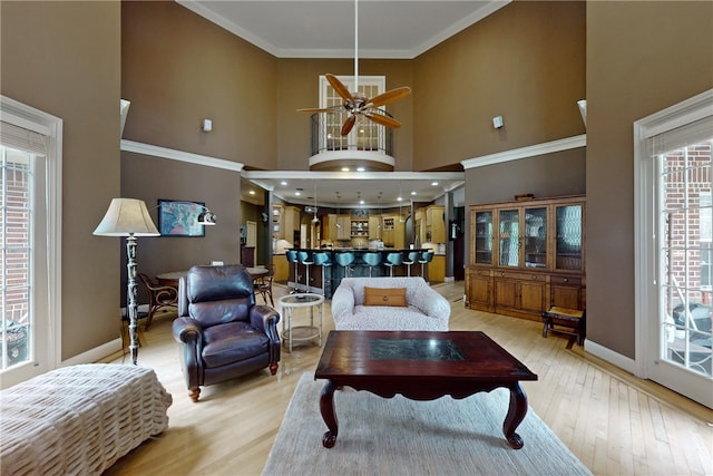 living area featuring a ceiling fan, baseboards, a high ceiling, and light wood finished floors