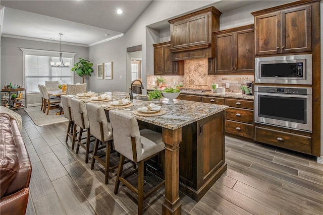 kitchen with hanging light fixtures, an inviting chandelier, vaulted ceiling, a center island with sink, and appliances with stainless steel finishes