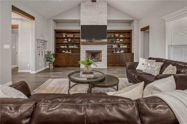 living room with built in shelves, dark hardwood / wood-style flooring, high vaulted ceiling, and a stone fireplace