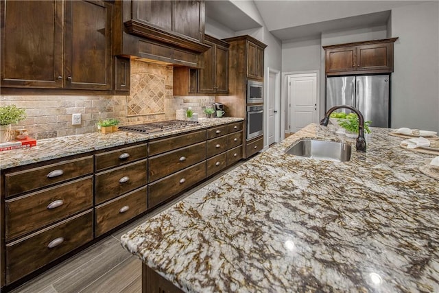 kitchen with light stone countertops, sink, stainless steel appliances, decorative backsplash, and dark brown cabinets