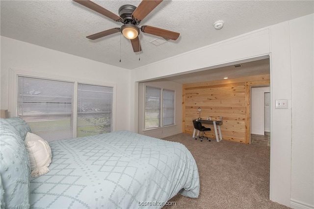 carpeted bedroom with ceiling fan, wooden walls, and a textured ceiling