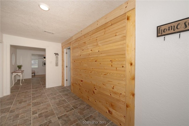 corridor featuring wooden walls and a textured ceiling