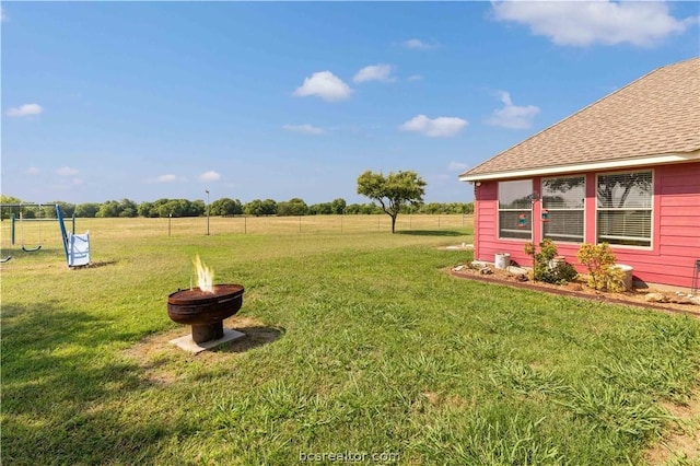 view of yard featuring a rural view, a playground, and an outdoor fire pit