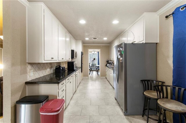 kitchen featuring tasteful backsplash, white cabinetry, ornamental molding, and appliances with stainless steel finishes