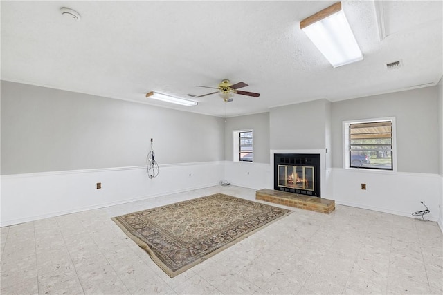 living room featuring a brick fireplace, a textured ceiling, ceiling fan, and a healthy amount of sunlight