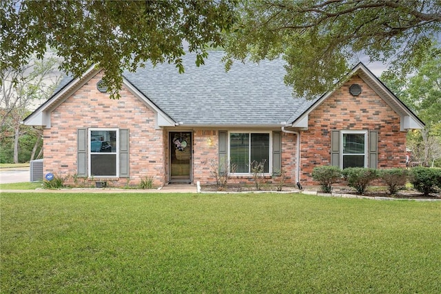 view of front of home featuring a shingled roof, a front yard, and brick siding