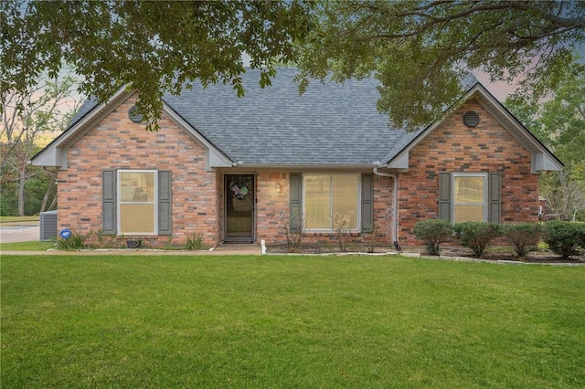 view of front of home featuring central AC unit, a front yard, a shingled roof, and brick siding