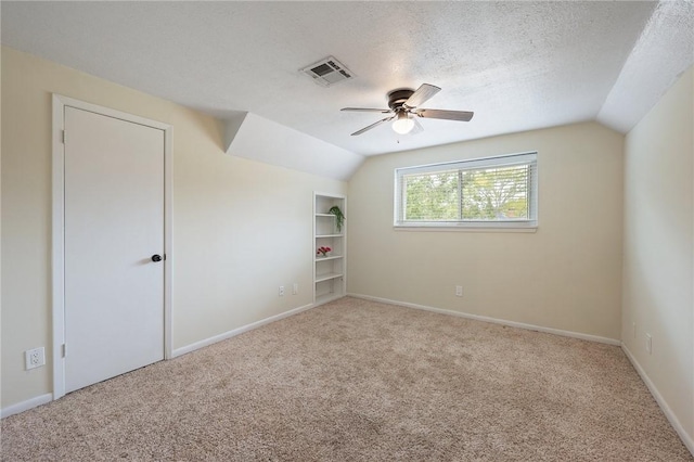 carpeted spare room featuring a textured ceiling, built in shelves, ceiling fan, and lofted ceiling