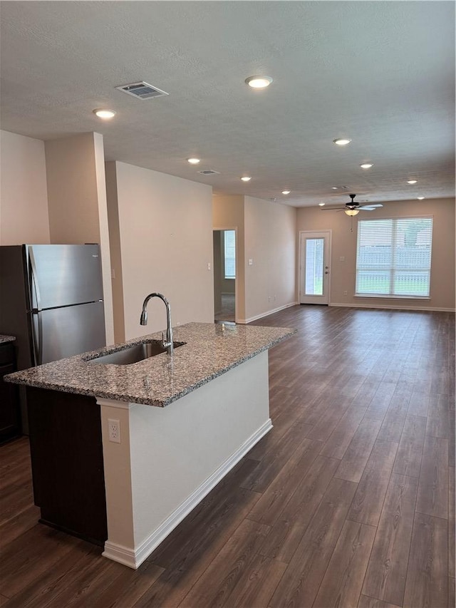 kitchen featuring visible vents, freestanding refrigerator, light stone countertops, dark wood-type flooring, and a sink