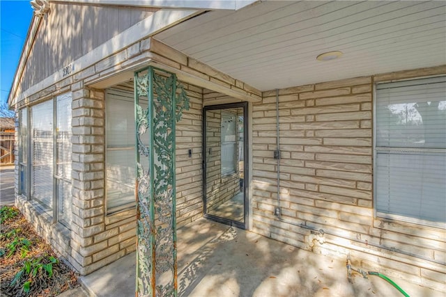 view of exterior entry with a patio and brick siding