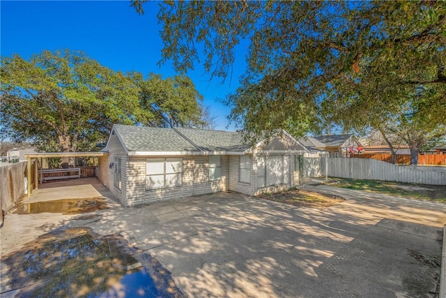 view of front of house featuring roof with shingles, a patio, concrete driveway, fence, and a carport