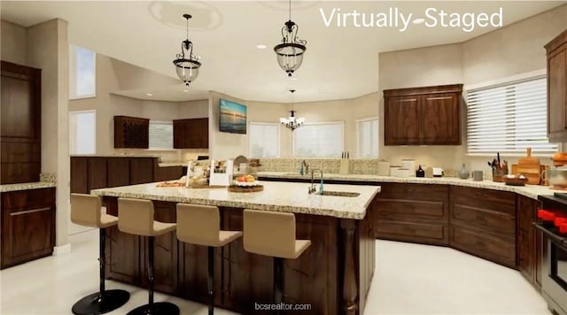 kitchen featuring a center island with sink, decorative light fixtures, light stone counters, range, and a chandelier