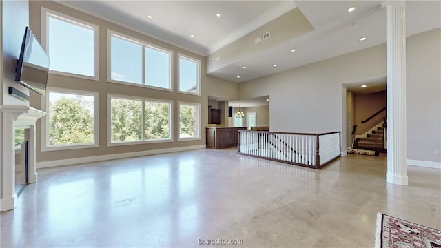 unfurnished living room with plenty of natural light, a towering ceiling, ornamental molding, and ornate columns