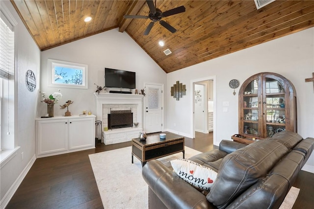 living room featuring a stone fireplace, beamed ceiling, ceiling fan, dark wood-type flooring, and wooden ceiling